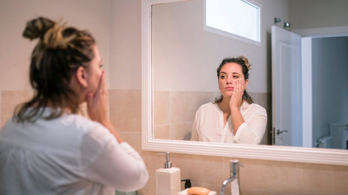 ¿El aceite de pescado es bueno para el eccema? 1 Mujer con eczema mirando en el espejo con aceite de pescado